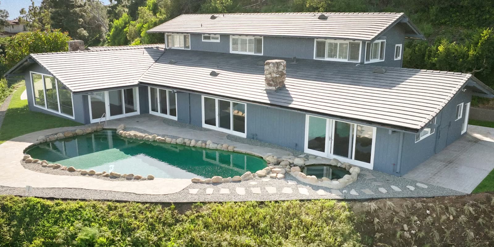 Aerial photograph of a grey 1960s ranch house with a kidney-shaped pool edged in boulders