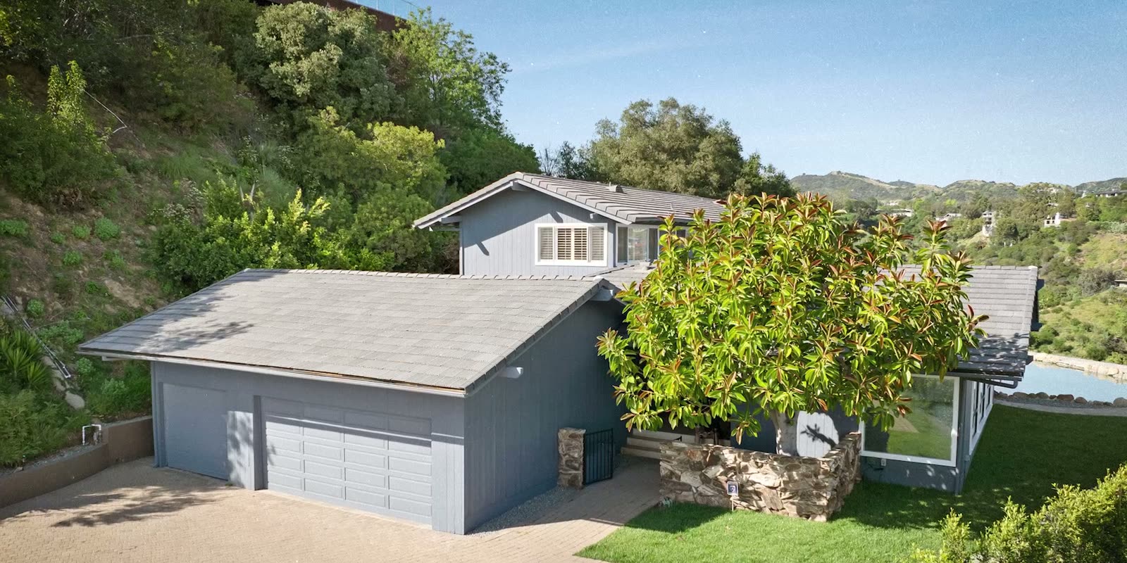 The ranch house's two-car garage and paver driveway beneath a mature tree