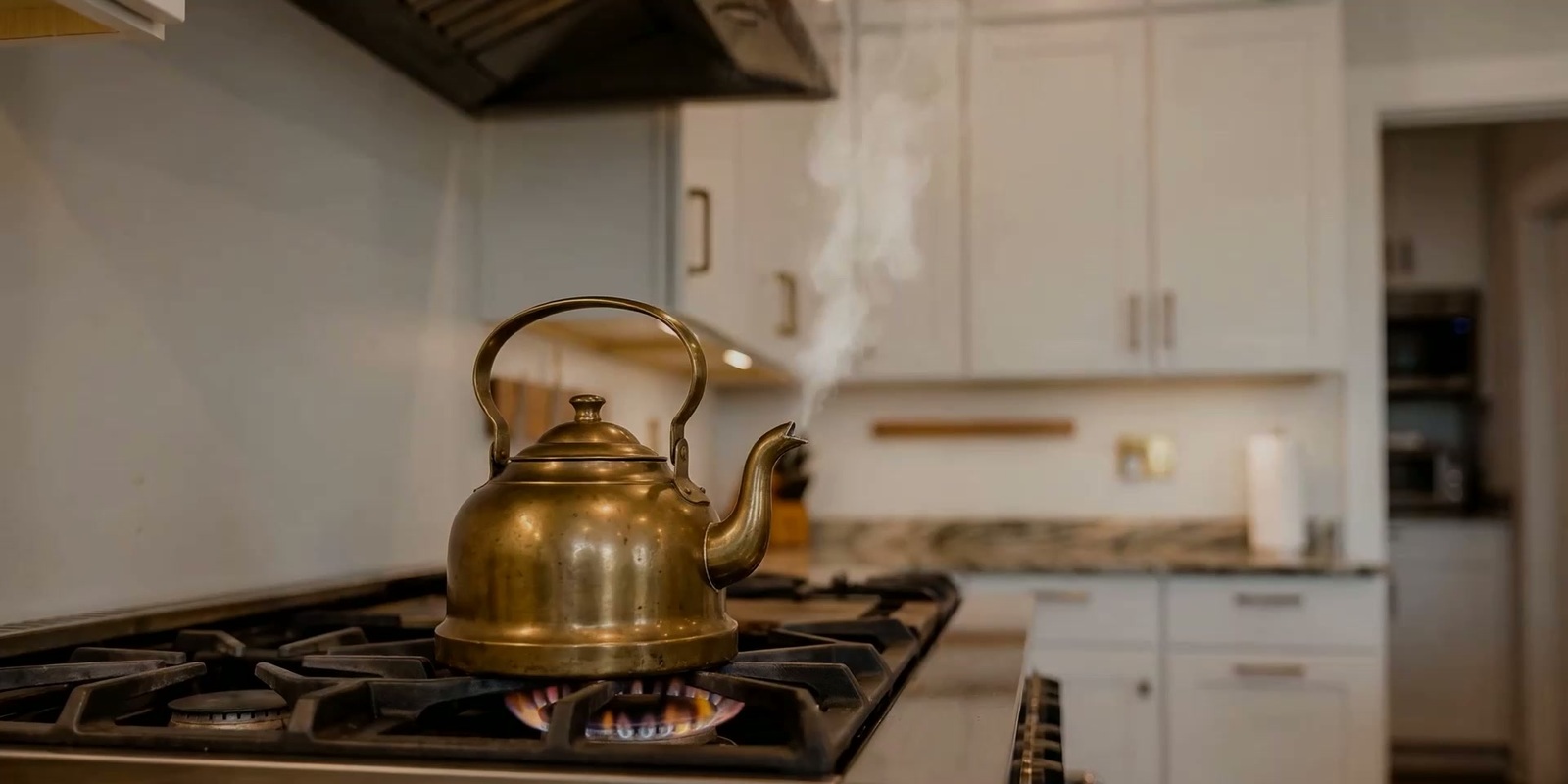 A brass kettle steaming on a gas stove in a bright kitchen