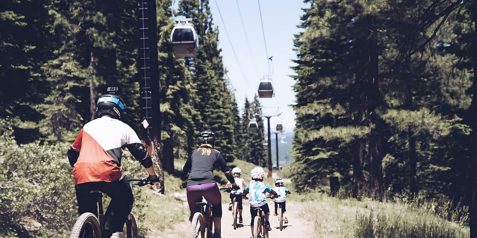 A family cycling along a forest trail beneath gondolas, in a scene from the film